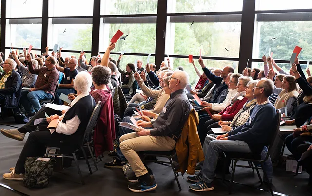 Bild von vielen Menschen in einer Halle die über etwas abstimmen